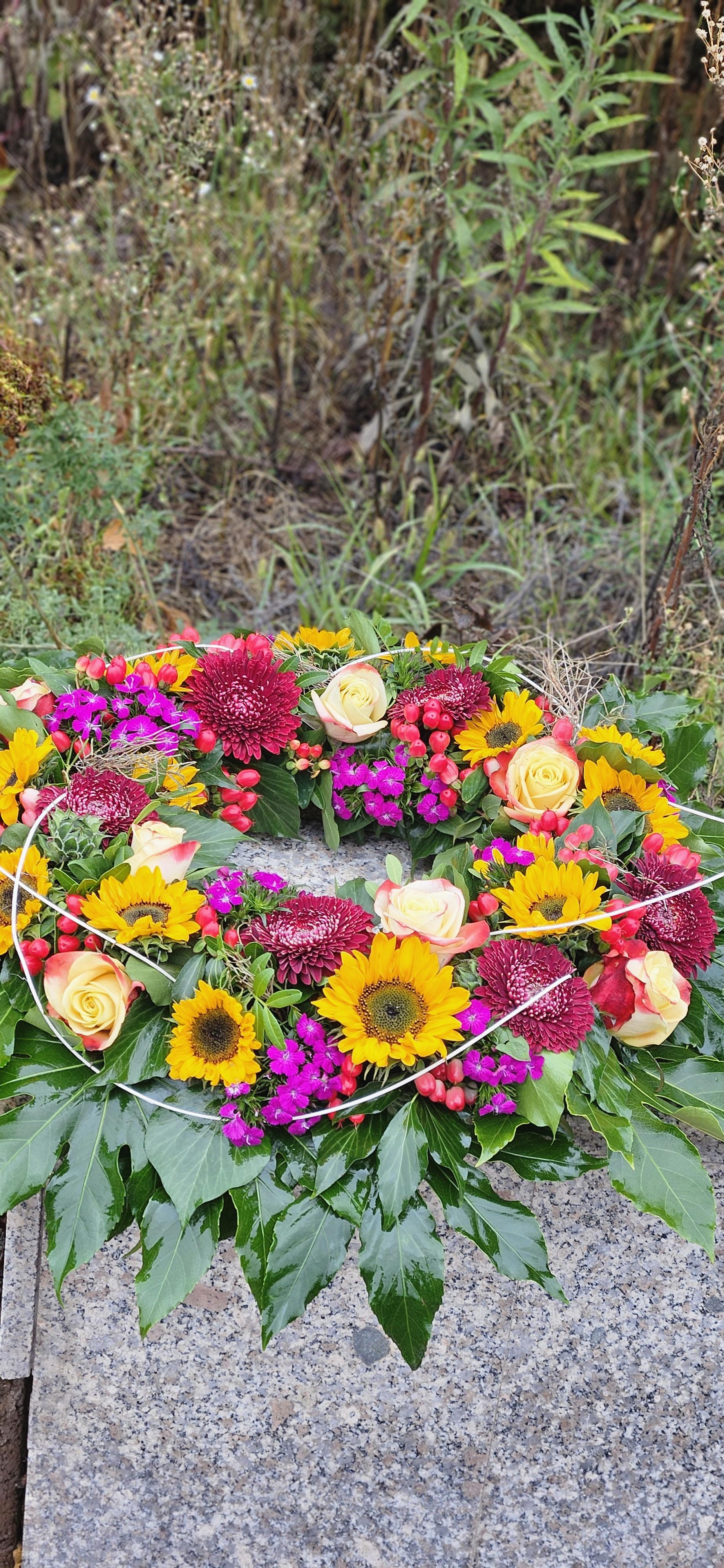 Trauerkranz mit Sonnenblumen Rosen und bunten Blueten auf Steinplatte