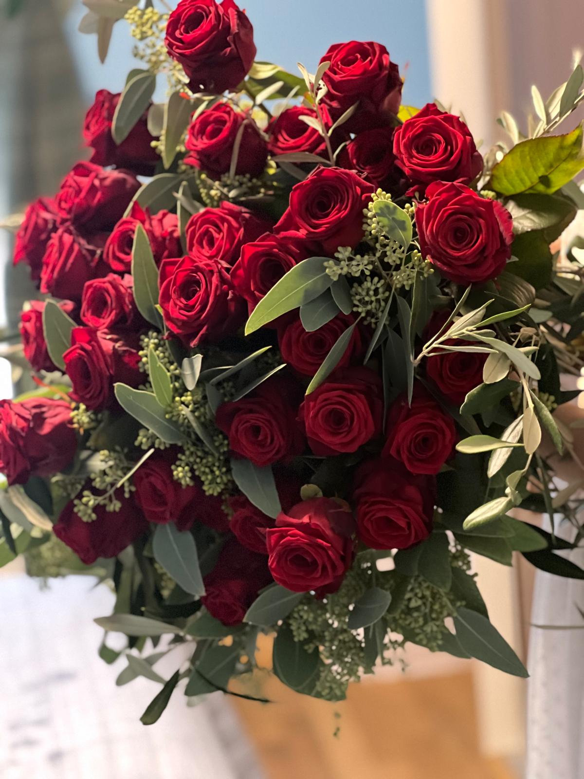 Ein uppiger Strauss roter Rosen mit gruenen Eukalyptuszweigen und Blaettern